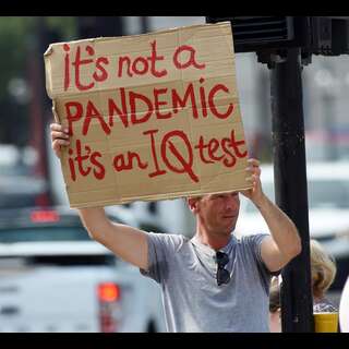 A gentleman holding a sign. Caption: It's not a PANDEMIC it's an IQ test.