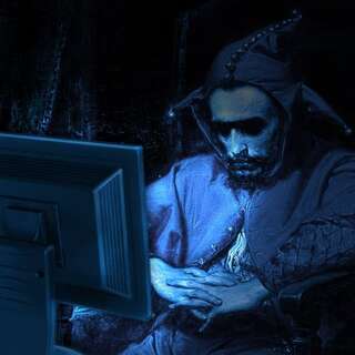 A medieval jester, solemnly being illuminated in blue hues by a monitor.